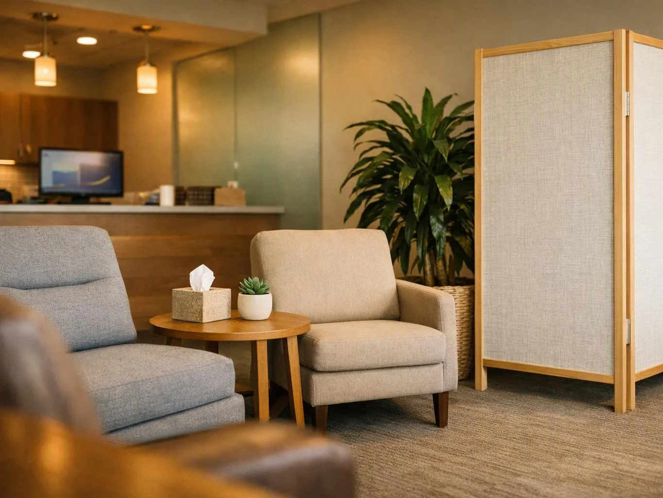 A quiet waiting area shows two chairs, a small round table, a plant, and a folding privacy screen