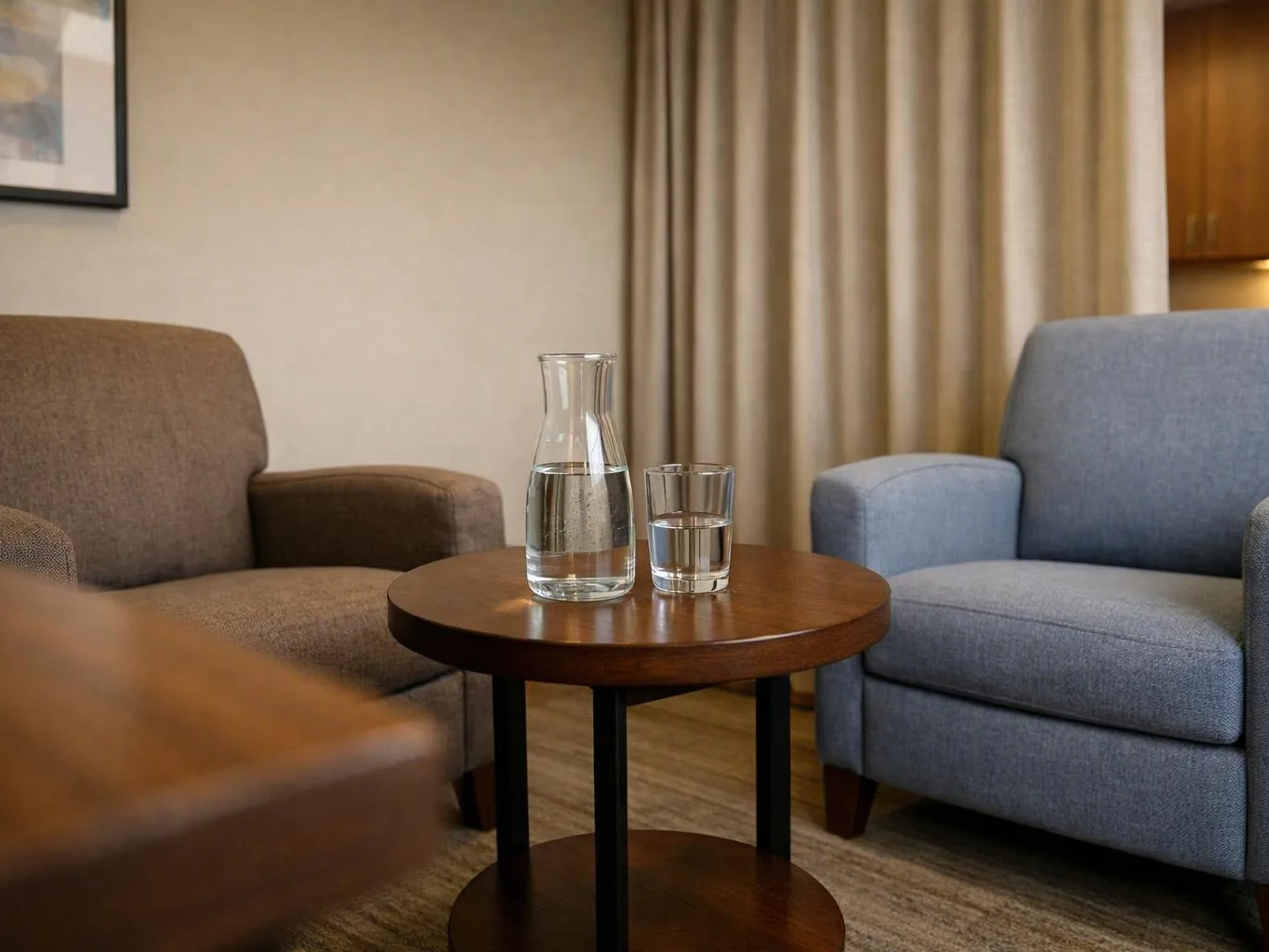 Two armchairs face a round wooden table with a water carafe and glass in a quiet room